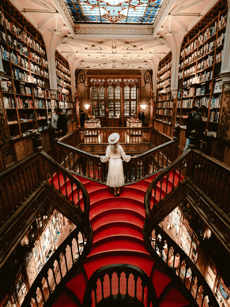 Stunning historic library with ornate woodwork, high ceilings, and a grand red-carpeted staircase.