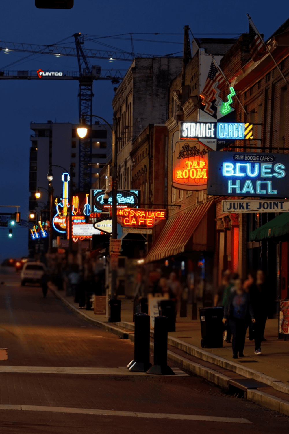 Colorful neon signs on a lively downtown street at night, showcasing bars, cafes, and entertainment venues.