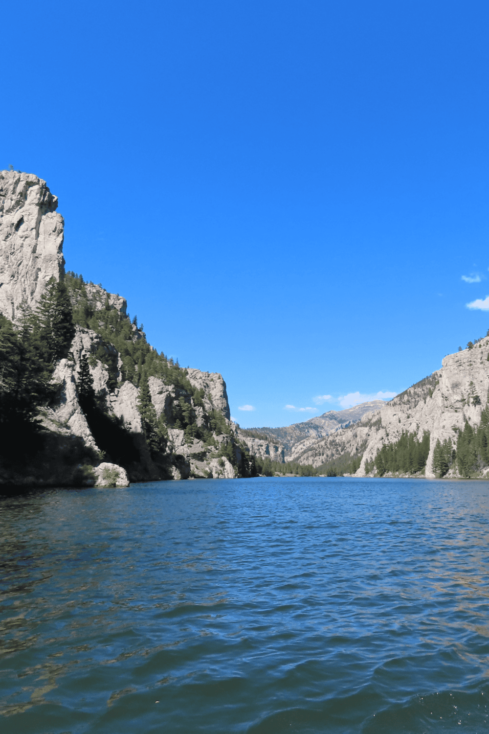 Serene mountain lake with cliffs and pine trees under a clear blue sky, ideal for nature exploration and outdoor adventure.