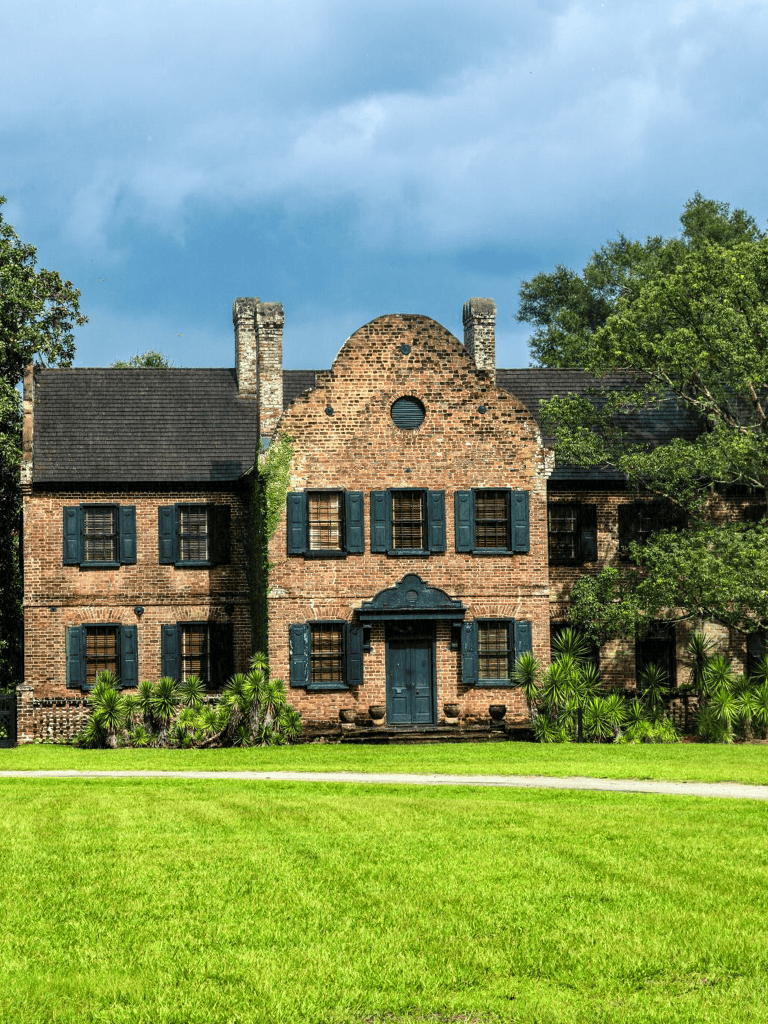 Historic brick house with black shutters and lush greenery, ideal for scenic house tours and architecture exploration.