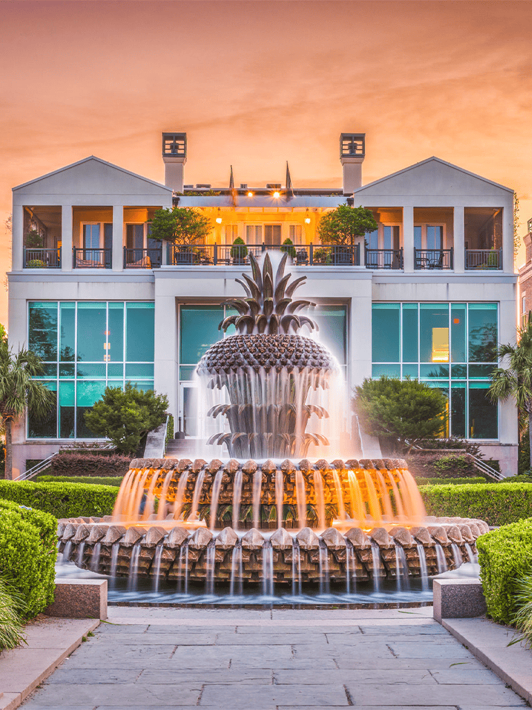 Elegant hotel with a pineapple fountain and lush greenery at sunset.