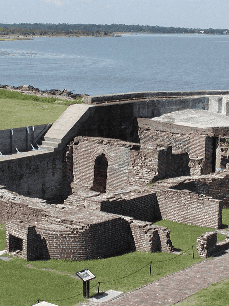Ancient brick fort ruins by waterfront, historical site with water view and grassy area.