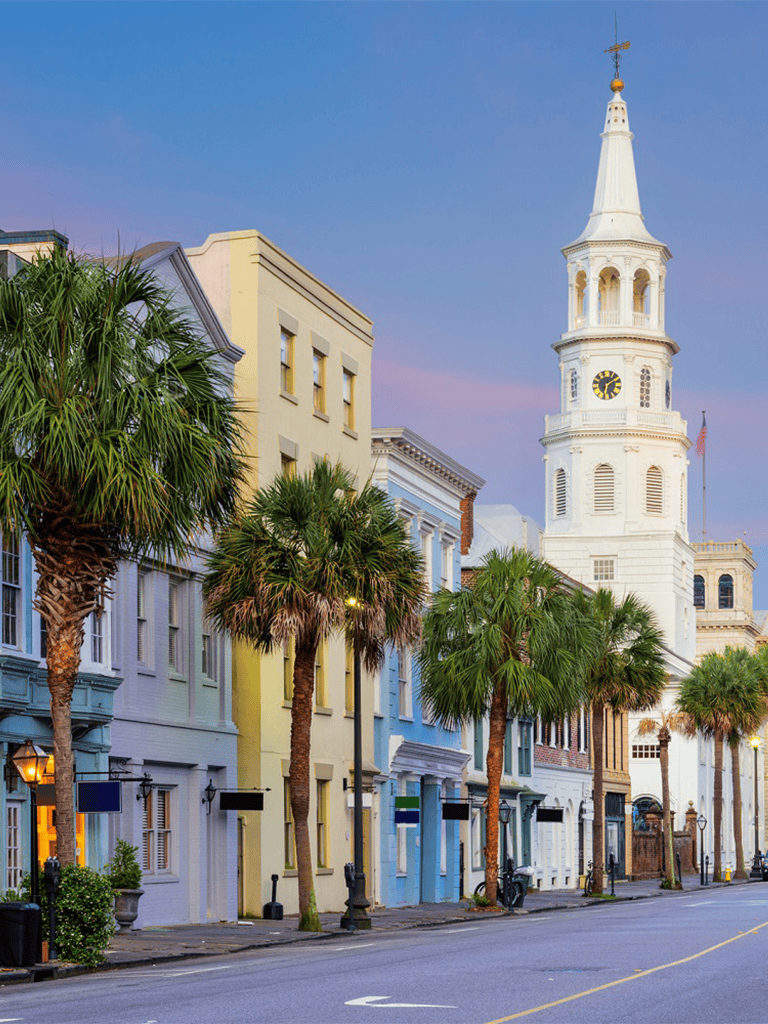 Colorful historic buildings with palm trees and a iconic church tower in Charleston, South Carolina.