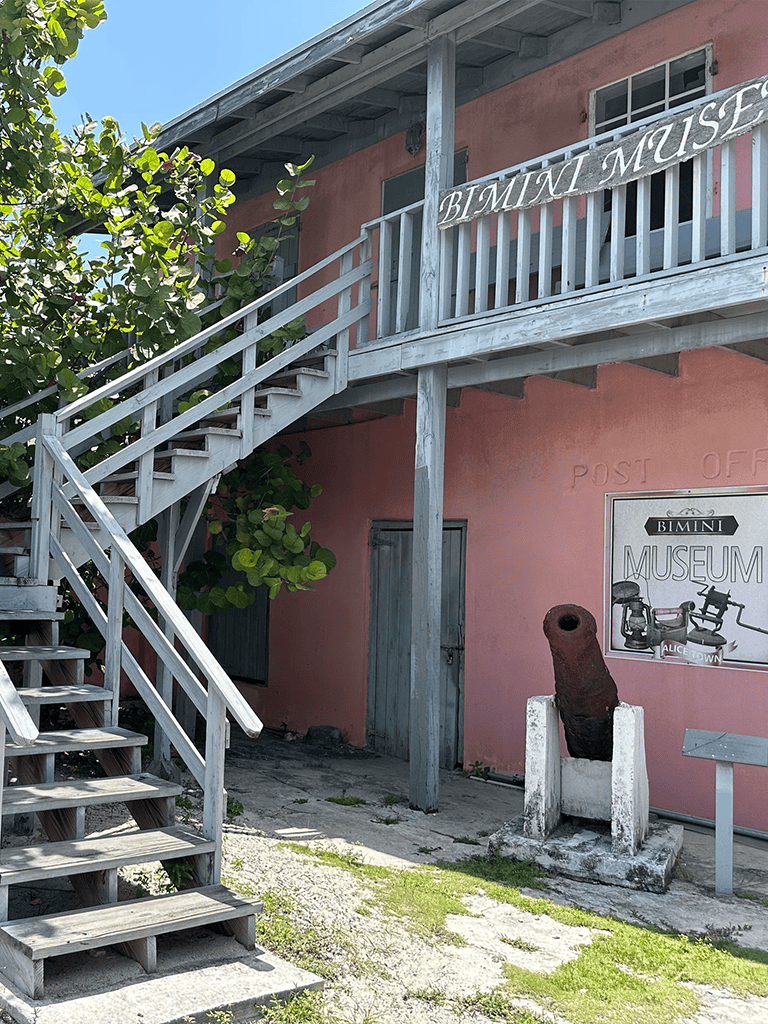 Rustic Bimini Museum building with outdoor wooden staircase and historic cannon display.