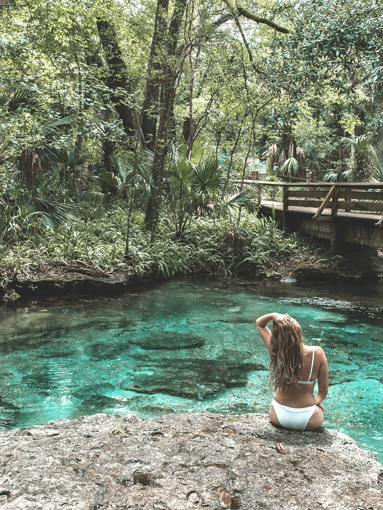 Refreshing natural spring in lush forest, woman relaxing at turquoise water.