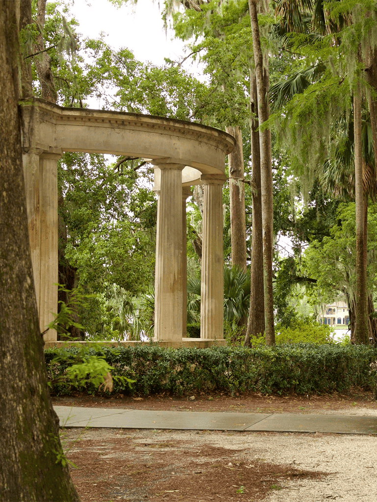 Ancient Greek-style garden ruins surrounded by lush green trees and foliage.