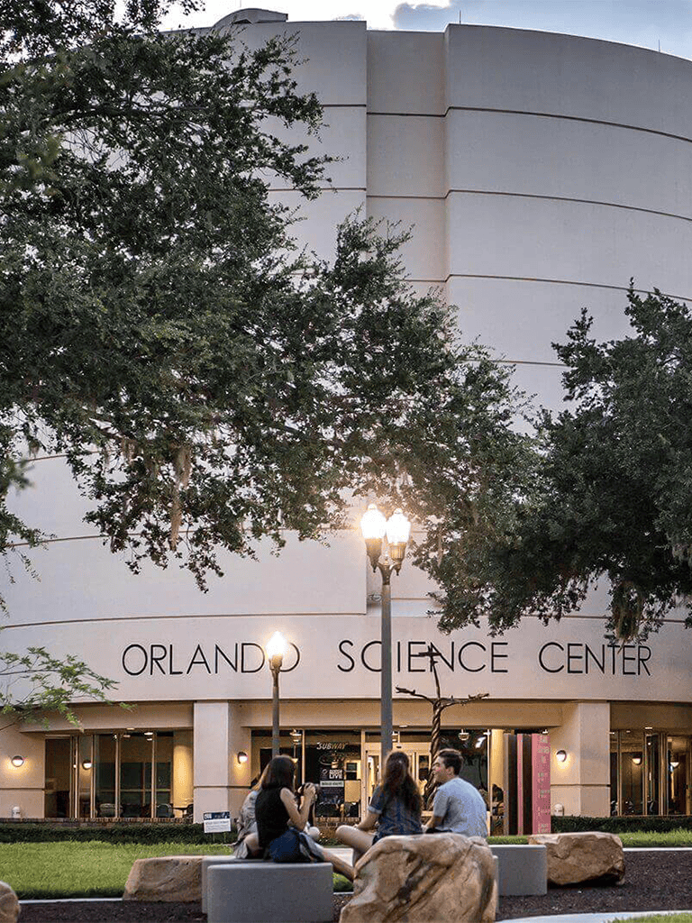 Modern science center building in Orlando with visitors sitting outside, ideal for science and educational attractions.