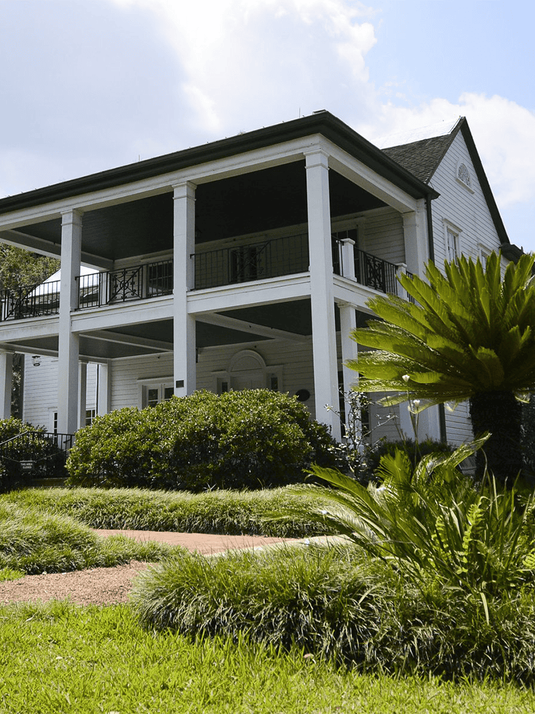 Elegant white residential house with lush landscaping and a spacious balcony, perfect for family living.