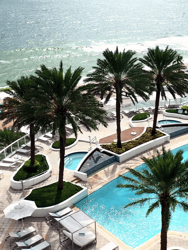 Luxurious hotel pool area with palm trees overlooking the ocean, perfect for relaxation and leisure.