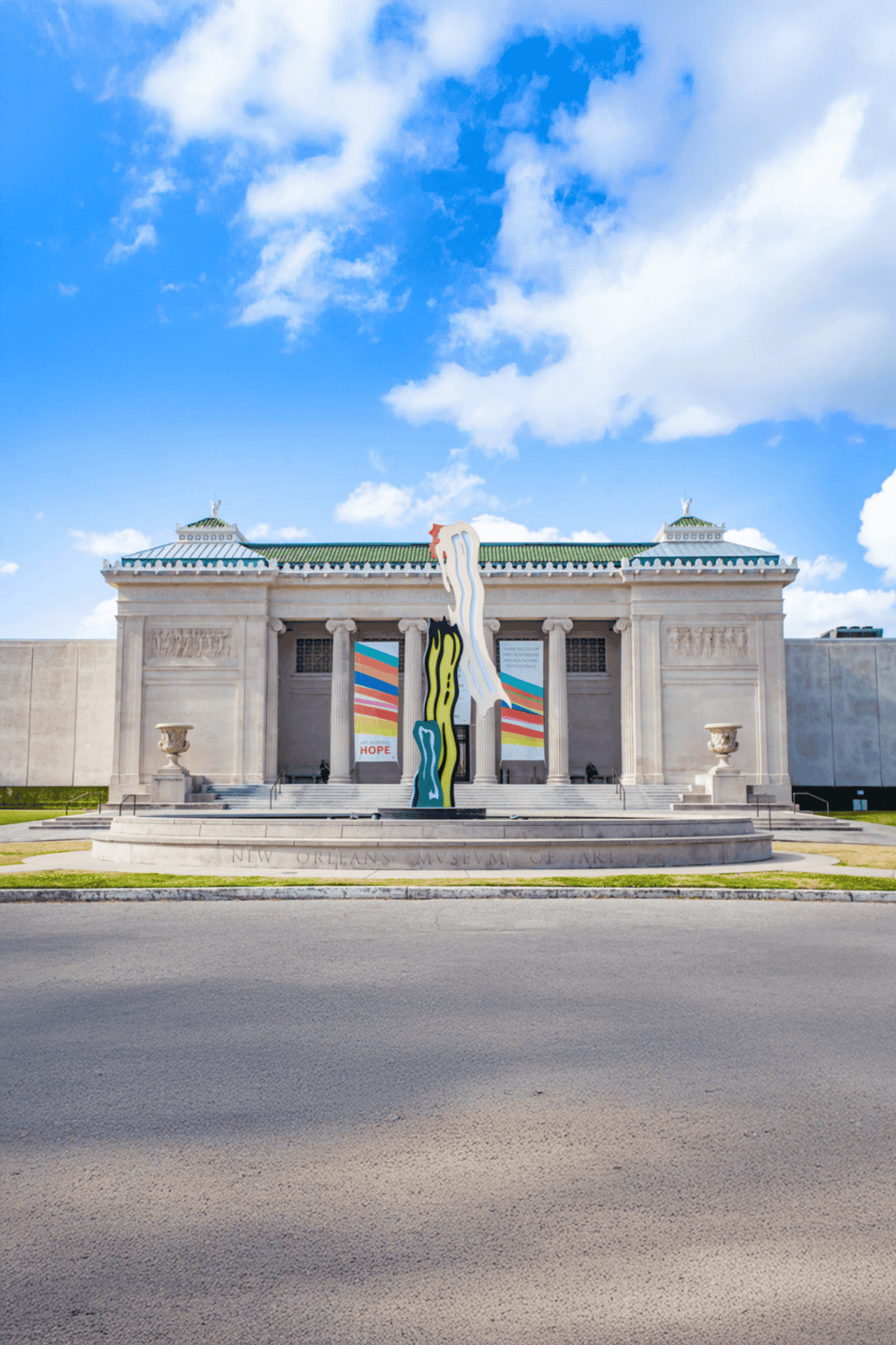 Colorful New Orleans Museum of Art building with mural art installation, architectural columns, and a blue sky background.