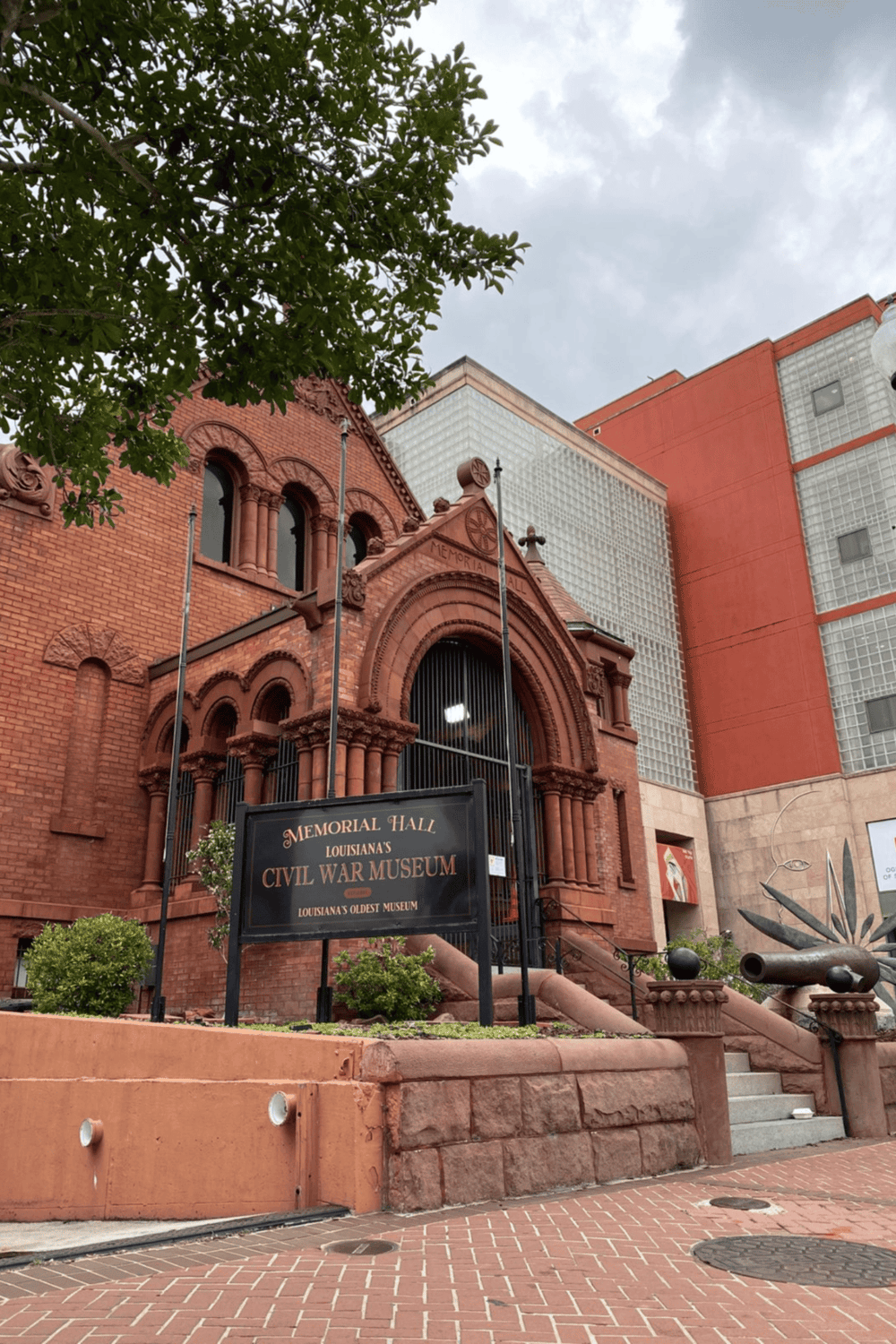 Weathered red brick memorial hall with "Civil War Museum" sign, historic architecture, and greenery, in downtown Louisiana.
