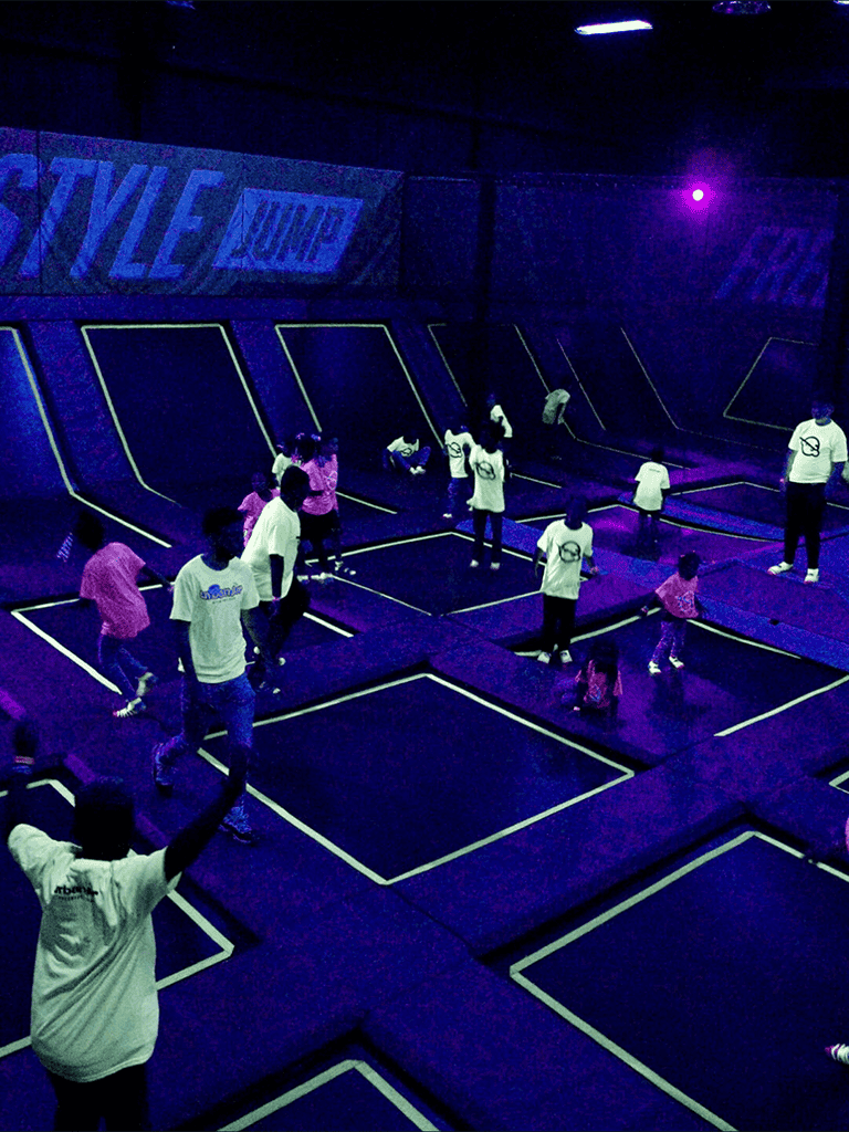 Brightly lit indoor trampoline park with children and adults jumping and having fun.