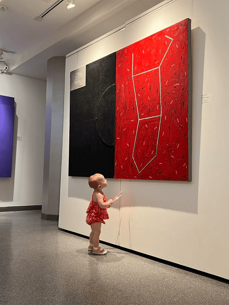 Colorful modern abstract art displayed in gallery with a curious young girl observing closely.
