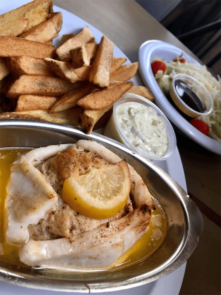 Grilled fish with lemon, fries, coleslaw, and dipping sauces at a casual restaurant.