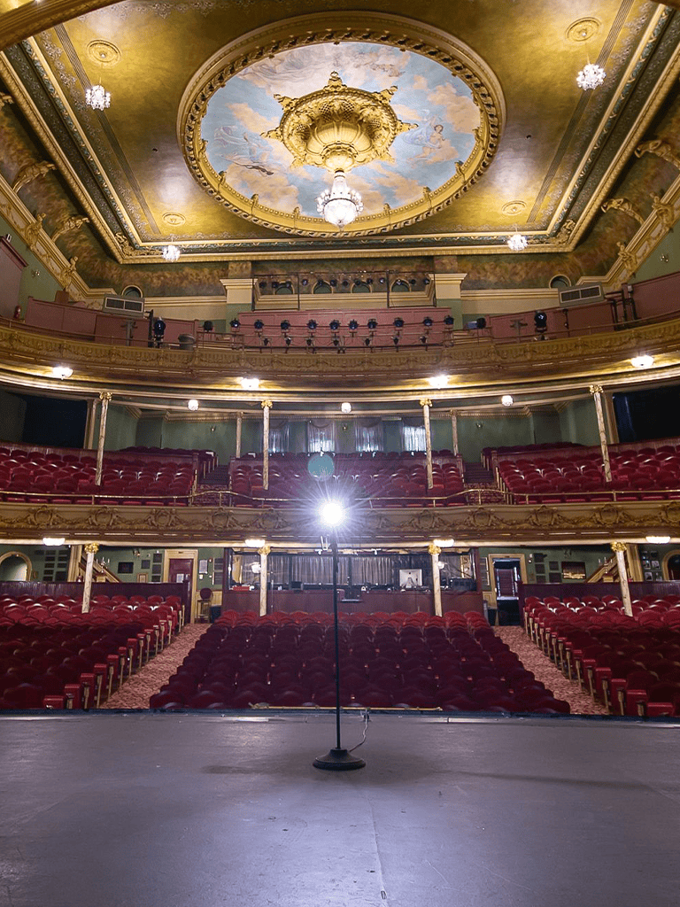 Elegant historic theater interior with ornate ceiling and plush red seats for live performances.