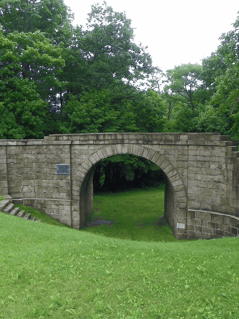 Ancient stone bridge surrounded by lush green trees, scenic outdoor location, historic architecture, peaceful natural setting.