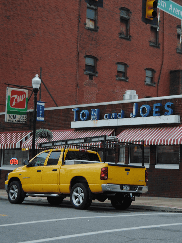 Yellow pickup truck parked outside Tom and Joes restaurant on a city street.