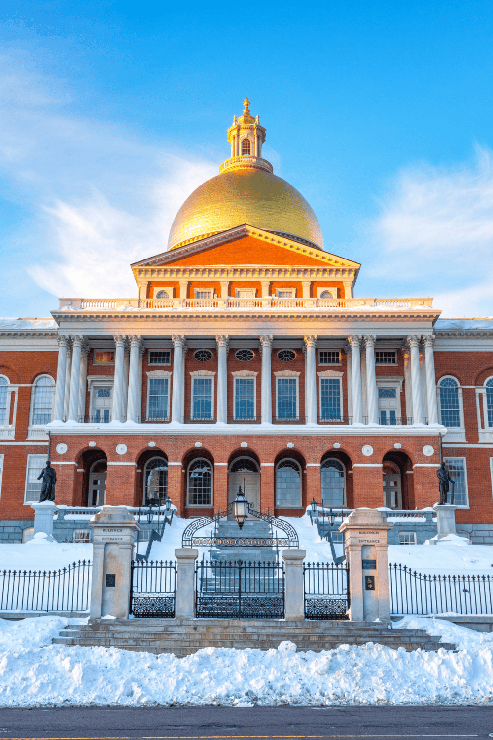 Historical Massachusetts State House with golden dome and snow-covered steps, Boston landmark, government building, and tourist attraction.