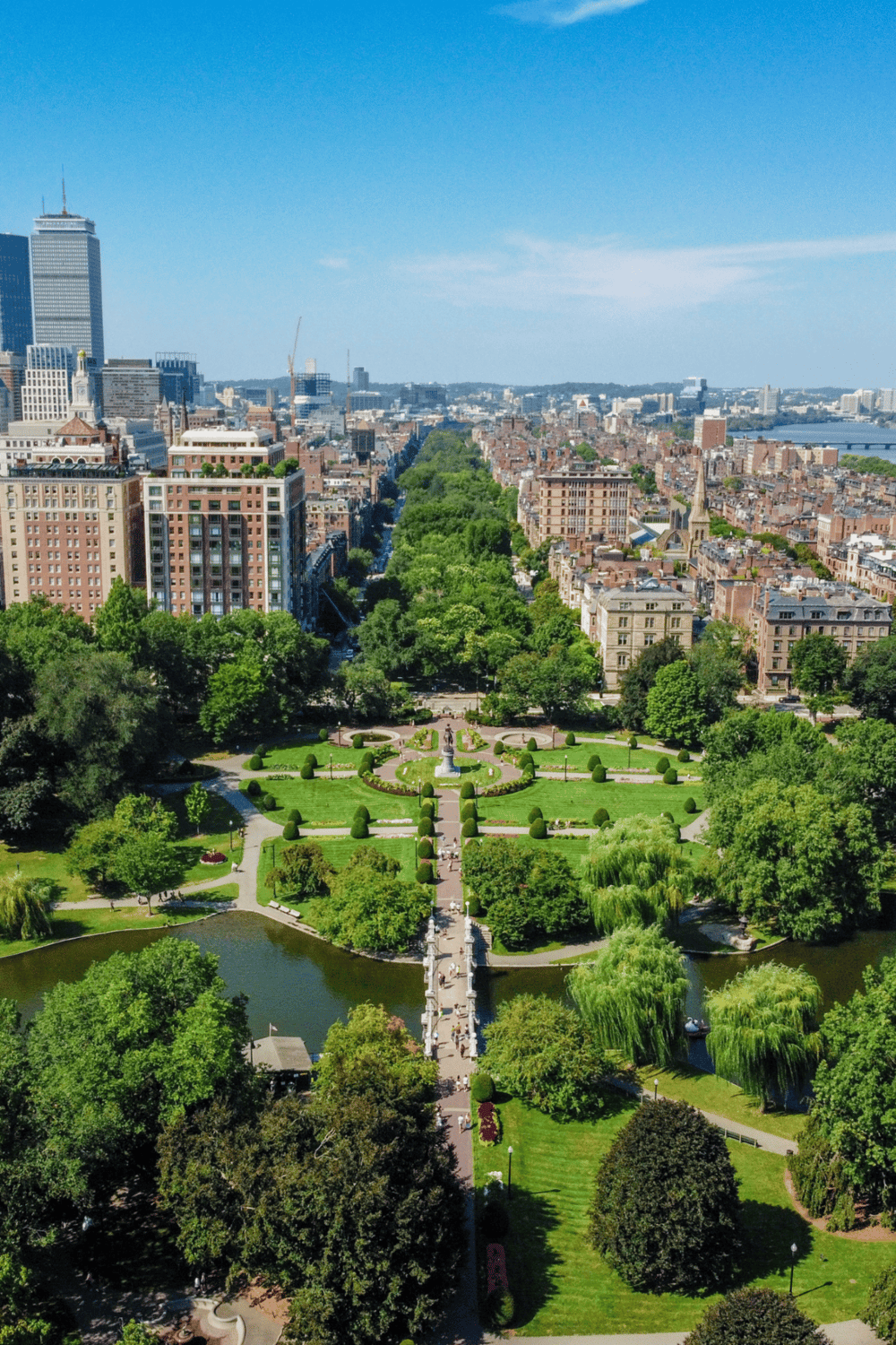 Lush green park with fountain in cityscape, downtown buildings, and river in background.