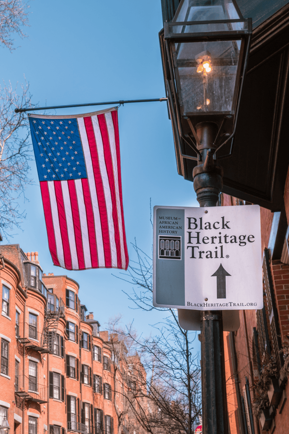 American flag on a streetlamp near historic buildings, promoting Black Heritage Trail tours.