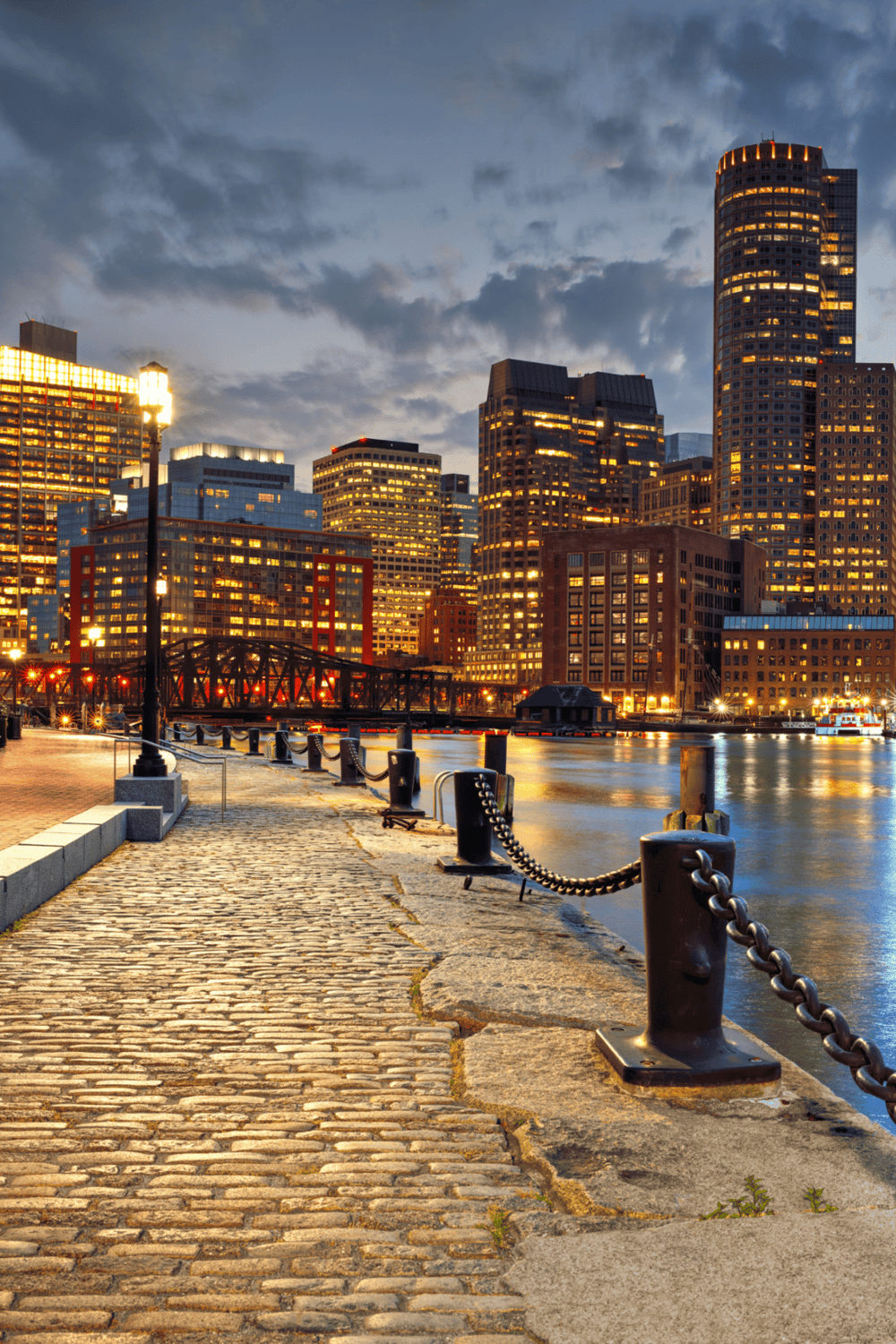 Downtown Boston waterfront at dusk with city skyline and cobblestone pier, scenic urban view.