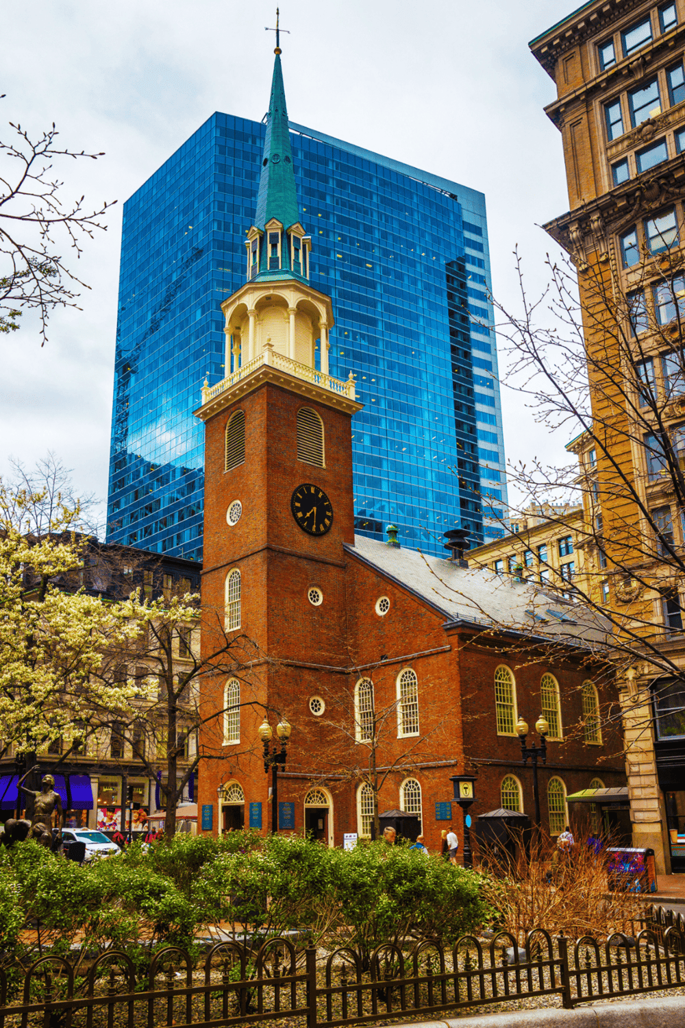 Historic church with a tall steeple surrounded by modern glass buildings in downtown area.