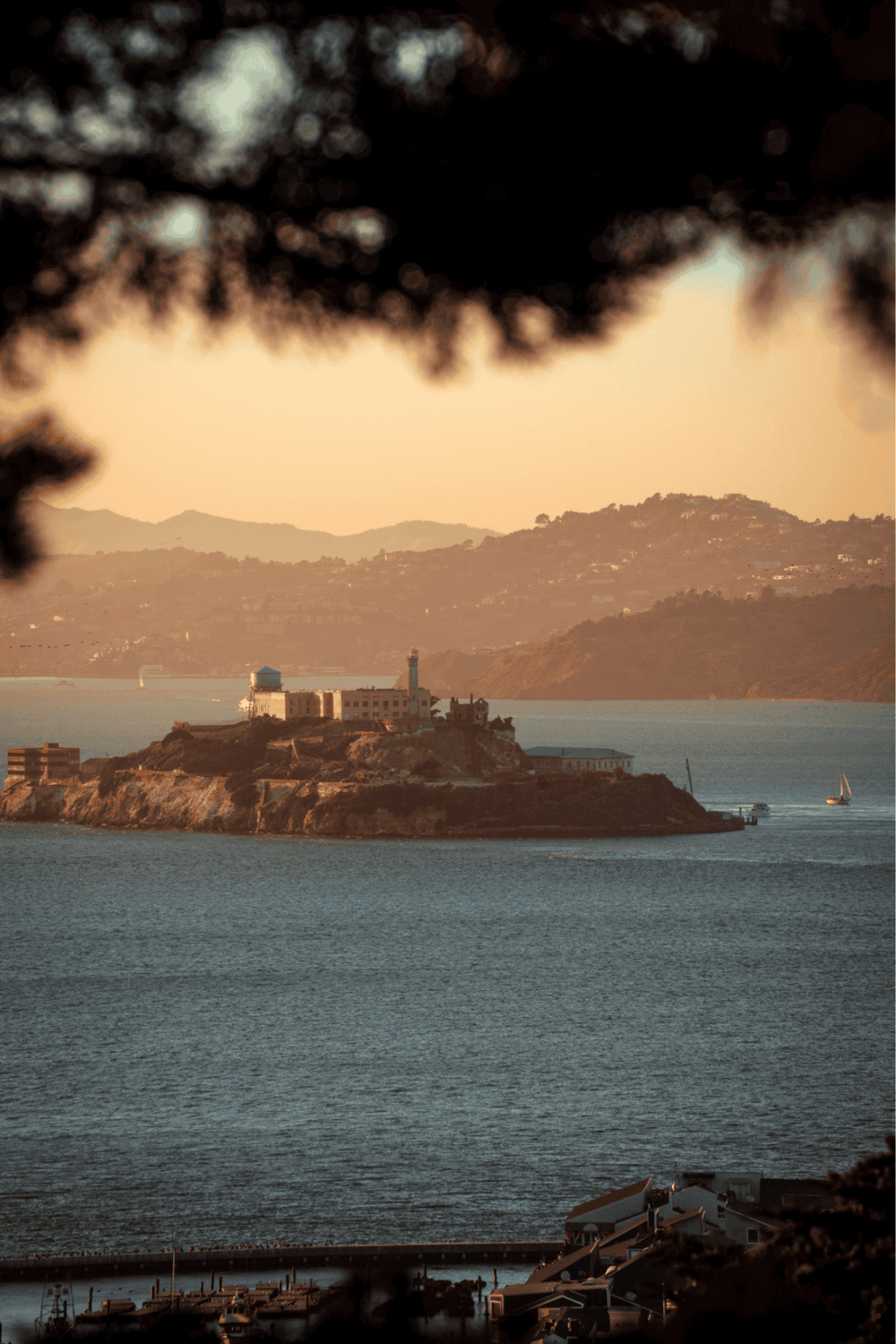 Clifton Lighthouse on Alcatraz Island at sunset, with San Francisco Bay in the background and scenic mountains.