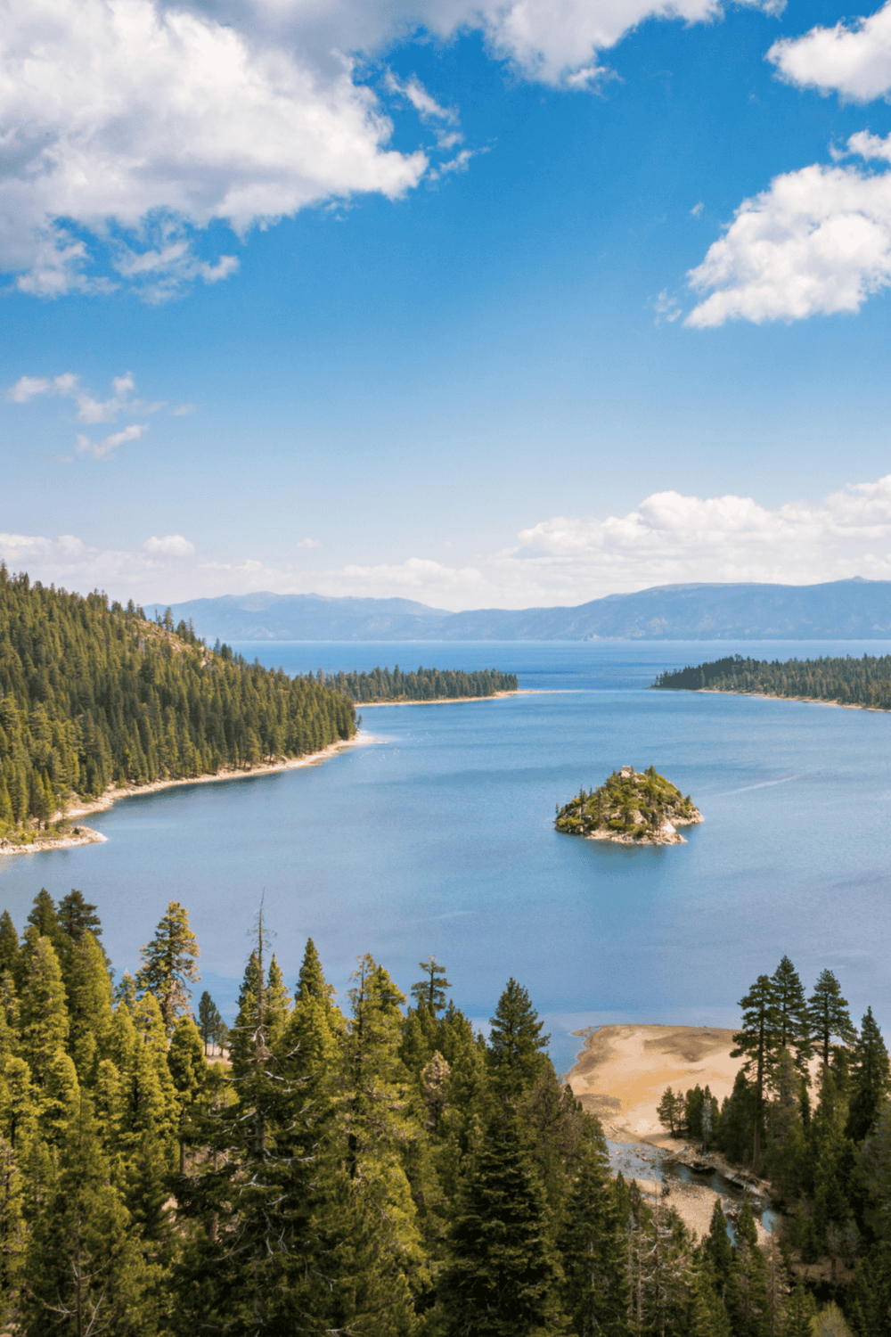 Serene lake with forested shoreline and small island, scenic mountain views, clear blue sky, nature travel destination.