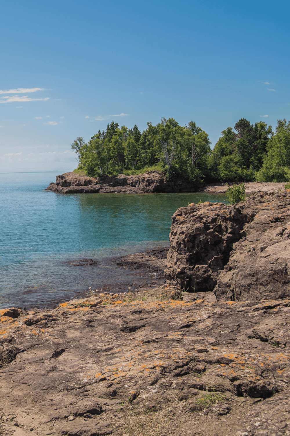 Scenic lakeside view with rocky shoreline, lush trees, and blue sky - perfect for outdoor adventure and nature exploration.