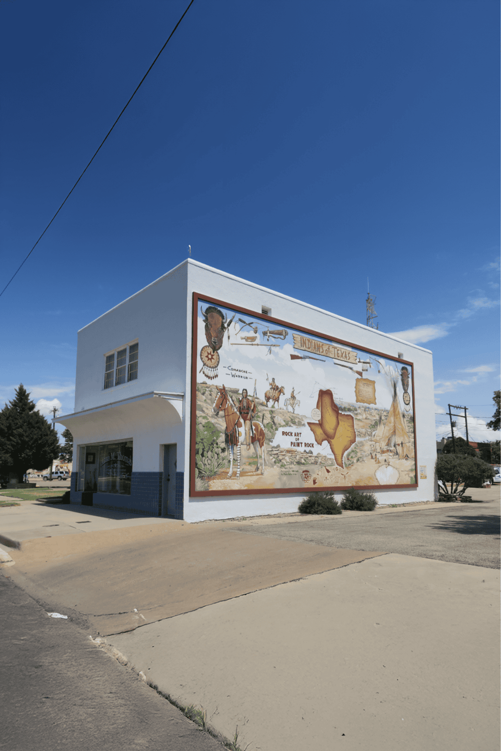 Colorful mural depicting Native American history and Texas culture on a small white building.