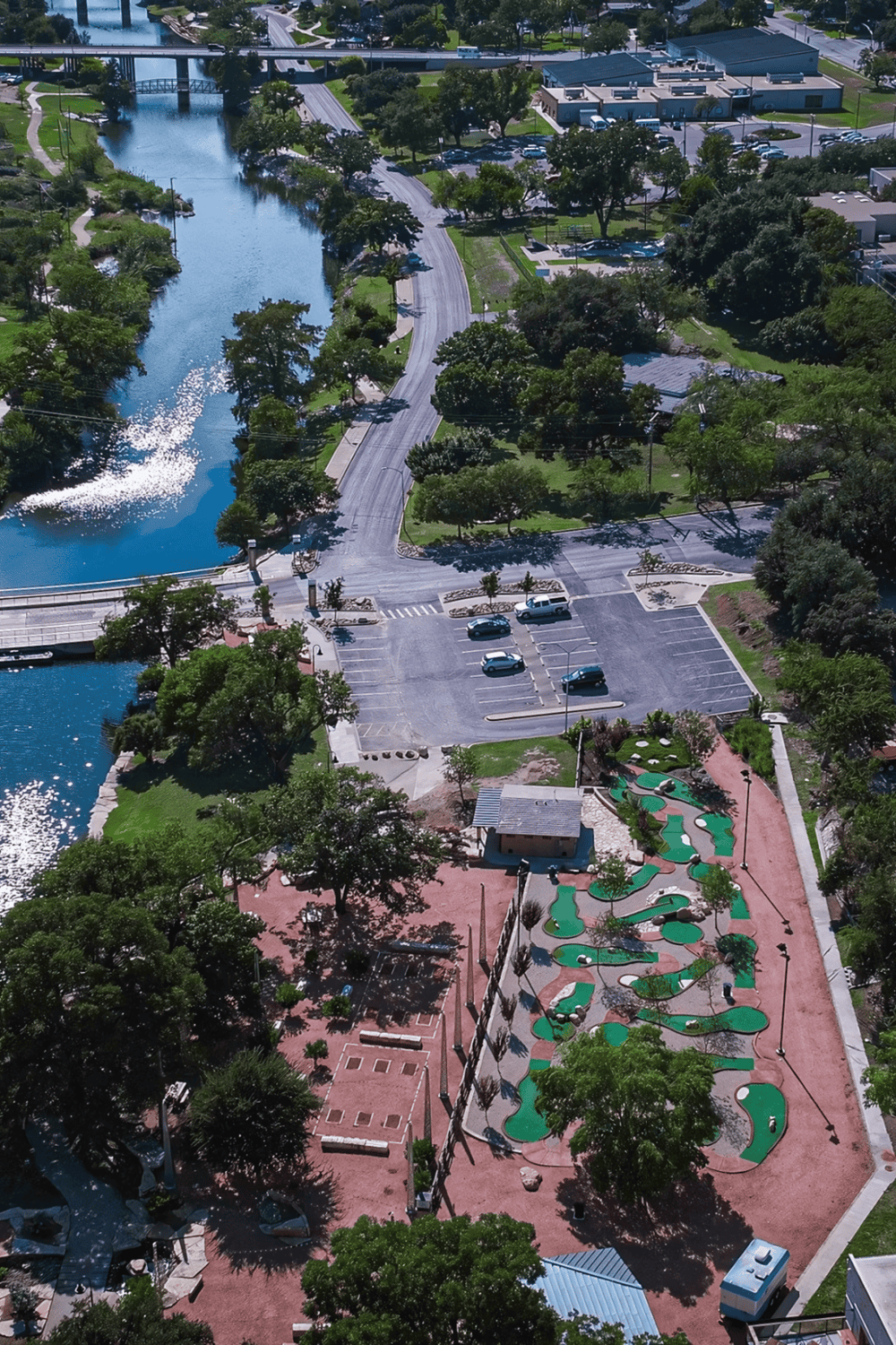 Vibrant park with mini golf, waterway, parking lot, and lush greenery in downtown area.