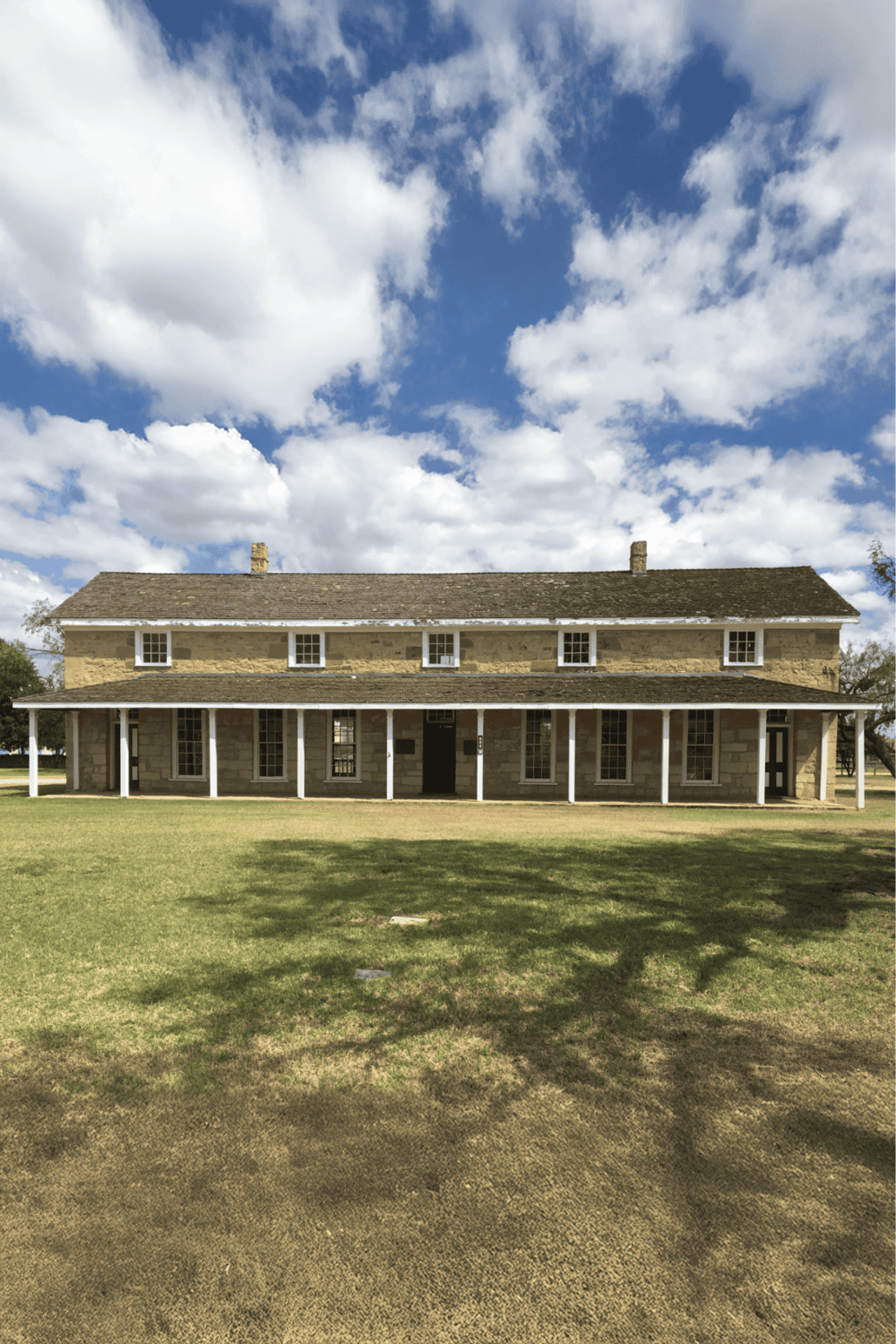 Historic stone house with white porch columns under a blue sky with clouds.