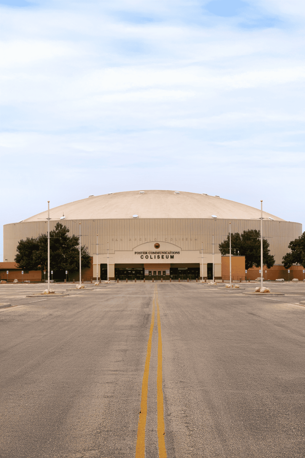 Stadium exterior at Foster Communications Coliseum in San Angelo, TX, with parking lot and trees.