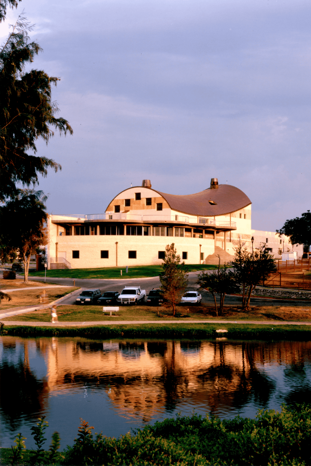 Contemporary building with curved roof and large windows near a pond, showcasing modern architecture and scenic surroundings.