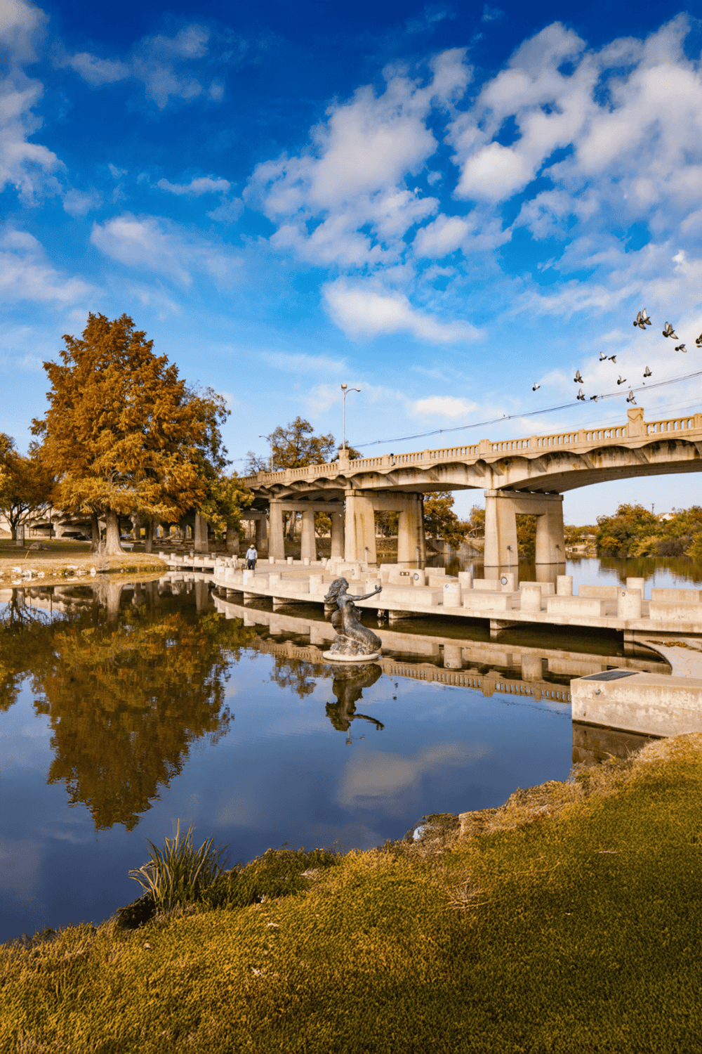Autumn park with bridge, water reflection, and statue, perfect for travel and navigation.