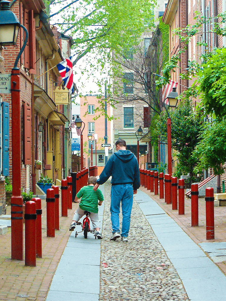 Cobbled street with colorful historic buildings, flag decor, and trees in downtown city area.