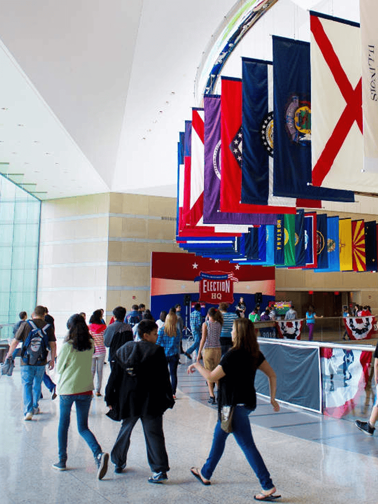Colorful flags hanging in a modern government building with young people exploring and walking around.