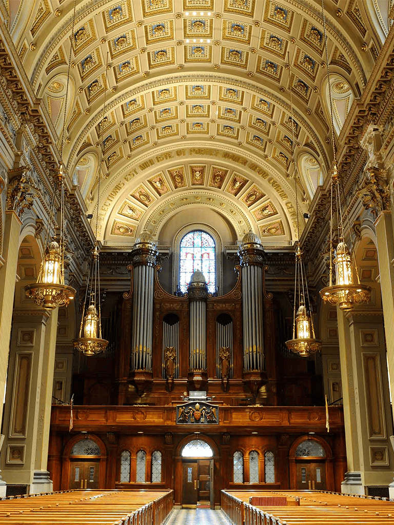 Intricate church interior with grand pipe organ, ornate ceiling, and stained glass window, representing historic architecture.