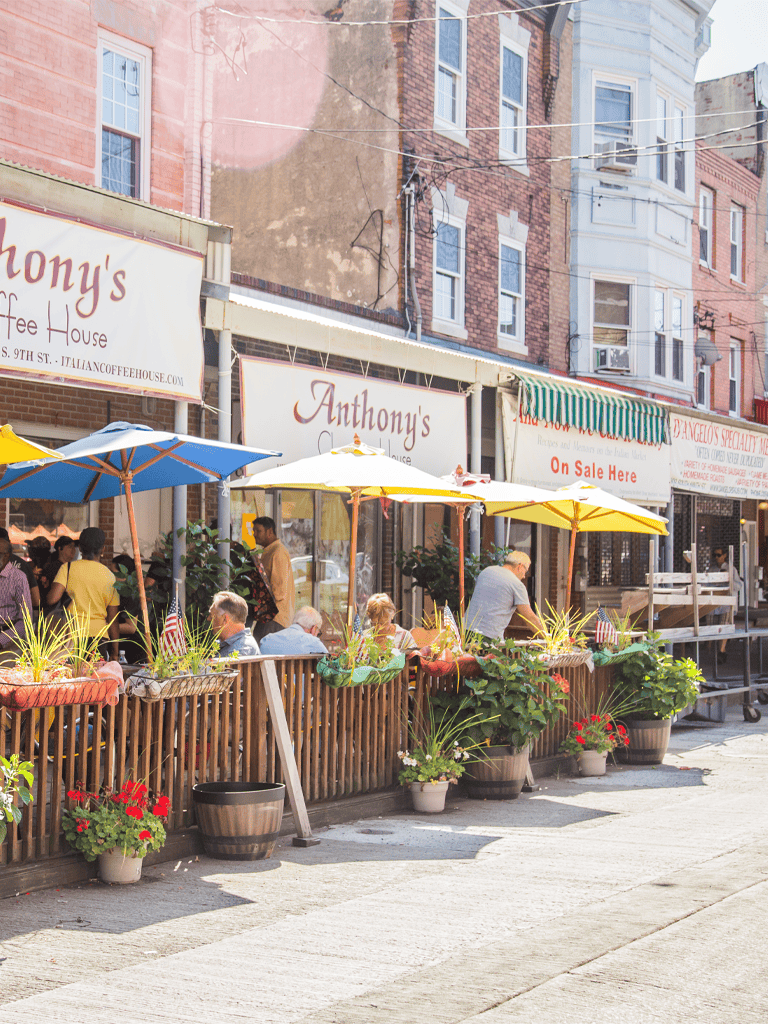 Outdoor dining at Anthony's Italian Coffee House with colorful umbrellas and vibrant potted plants in an urban neighborhood.