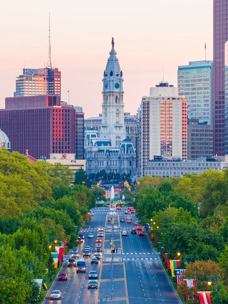 Historic Philadelphia City Hall with busy city street and skyline at sunset, prominently featuring Independence Hall.