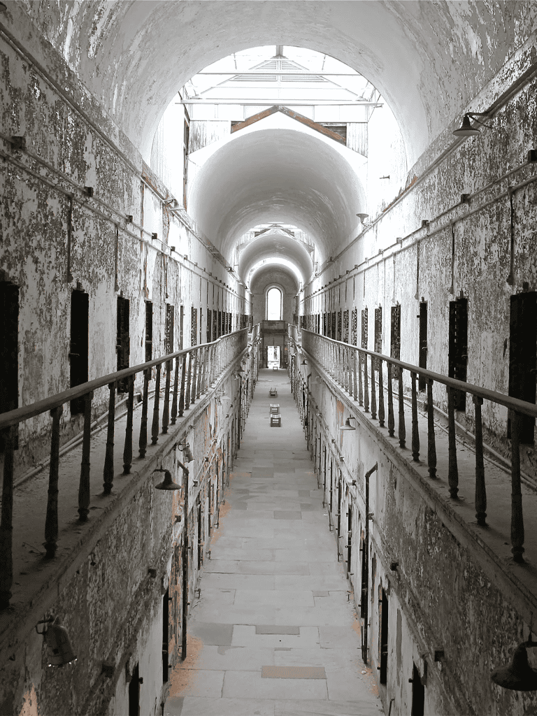 Empty historical prison corridor with multiple cell doors and arched ceilings, captured in black and white.