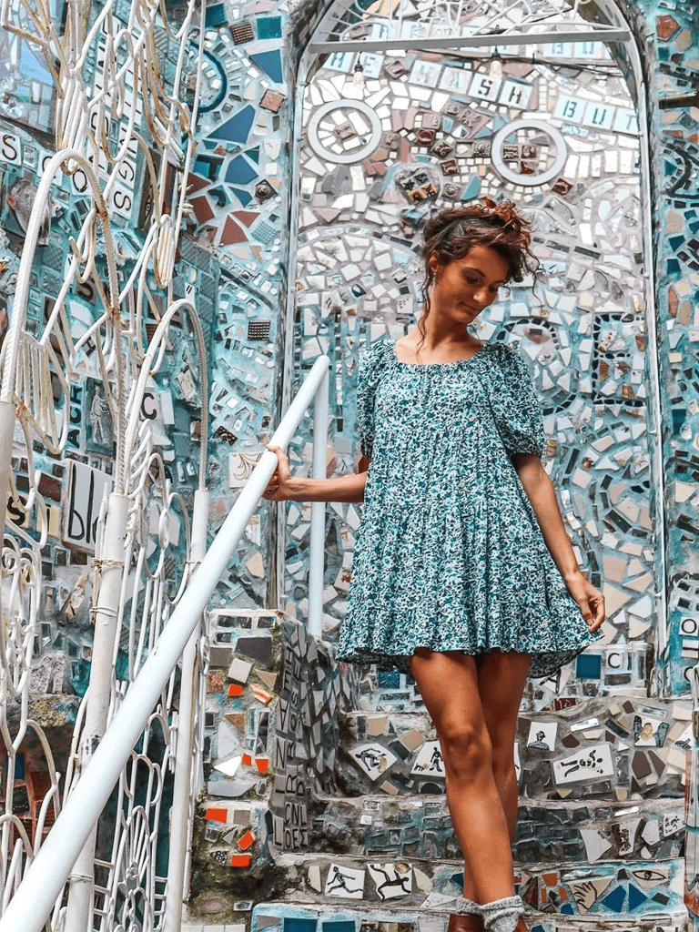 Colorful mosaic wall with clock motifs and a woman in a patterned dress on the stairs.