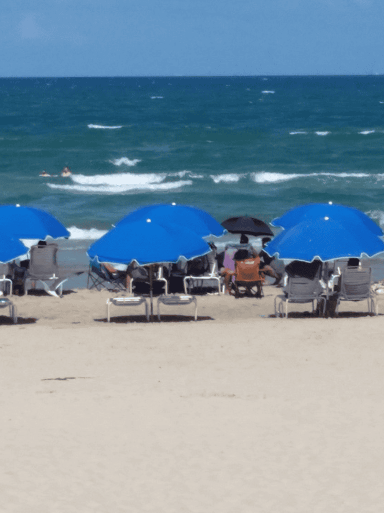 Sunny beach with blue umbrellas, lounge chairs, and ocean waves, perfect for a relaxing seaside getaway.