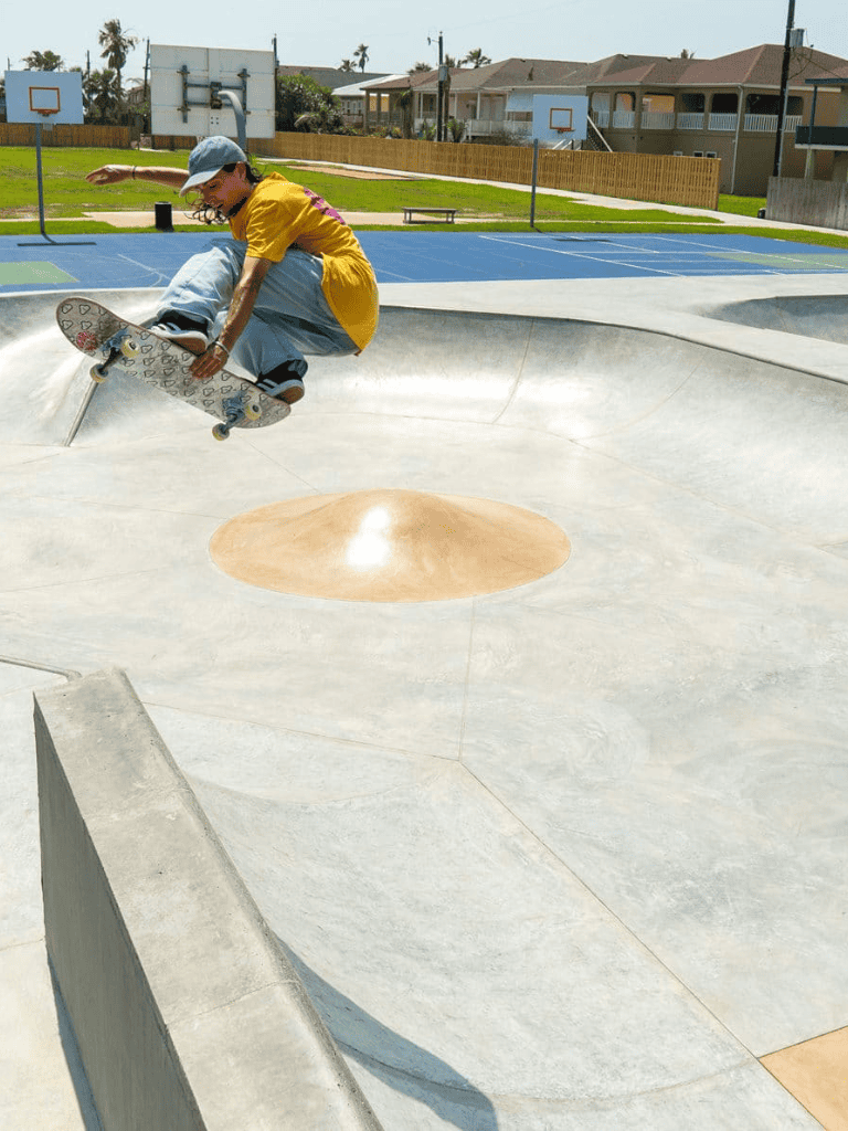 Skateboarder performing tricks at outdoor skate park with ramps and bowls.