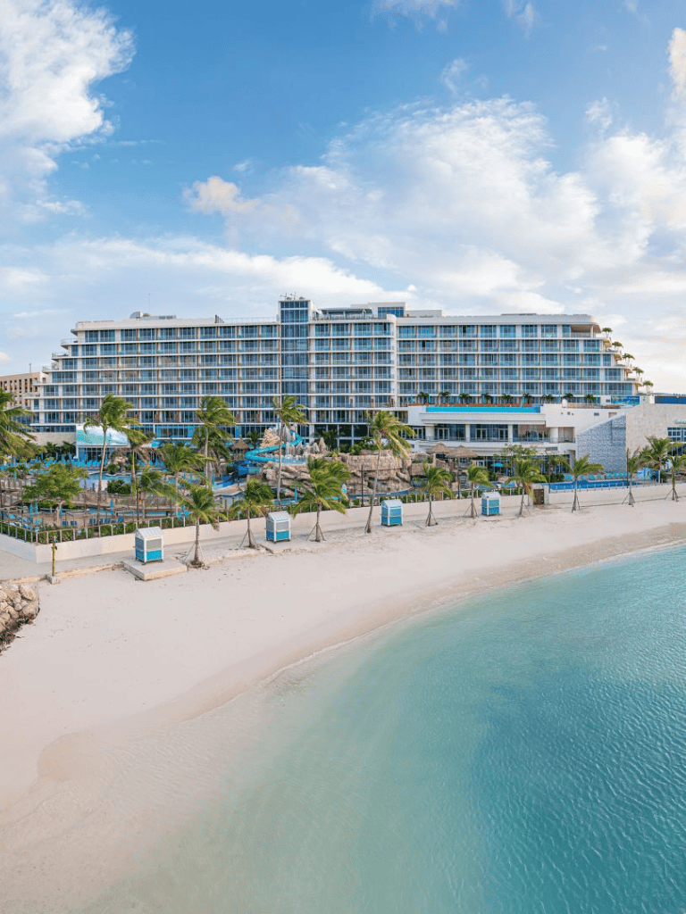 Luxurious beach resort on turquoise ocean with palm trees and clear sky in the background.