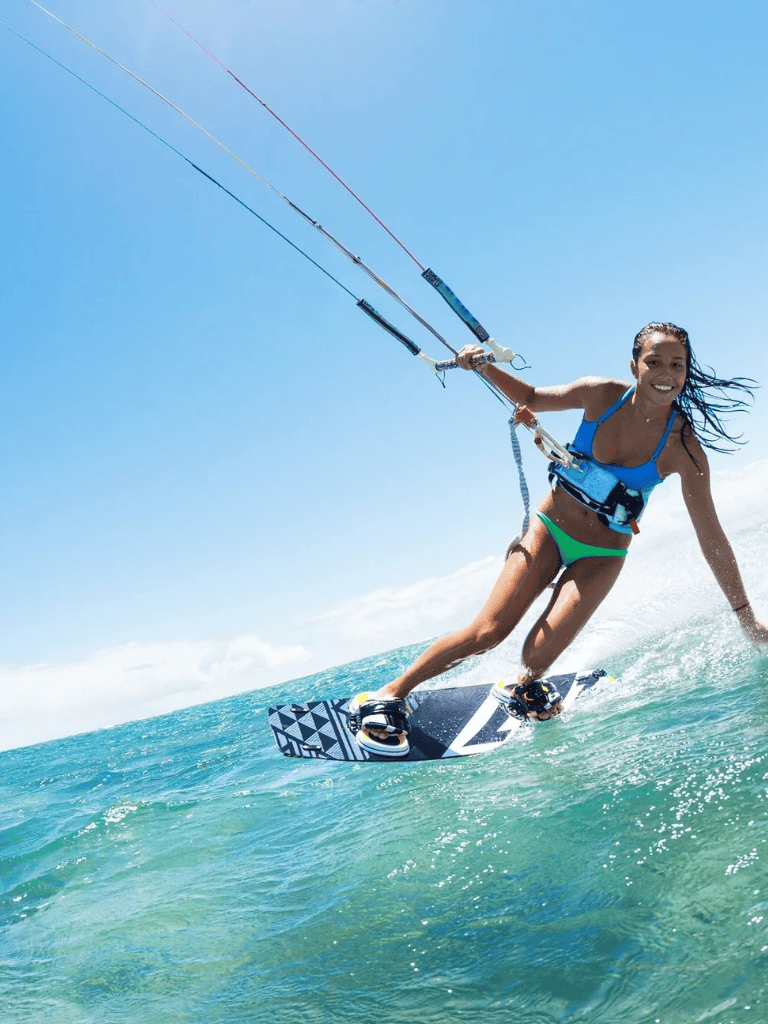 Kiteboarding on clear blue ocean water with a smiling female rider in a blue top and green bikini bottom.