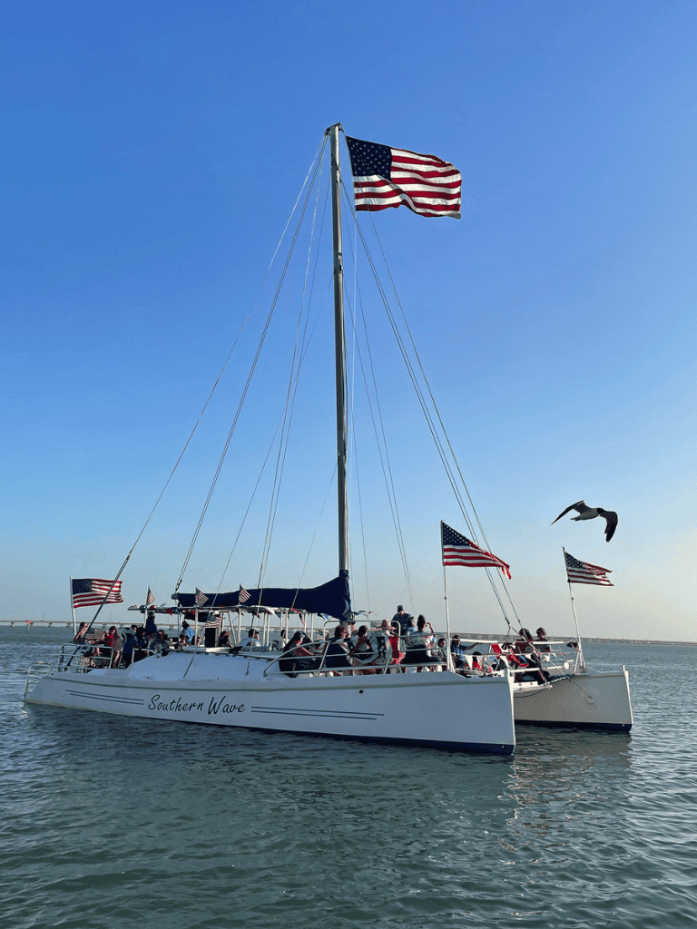 American flag on boat with people enjoying a boat ride on water, clear blue sky.