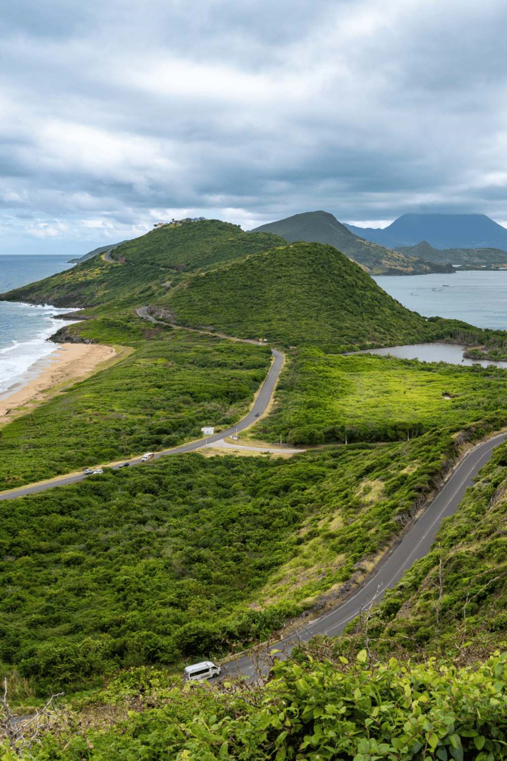 Rolling coastal landscape with winding roads, lush greenery, and mountain backdrop.