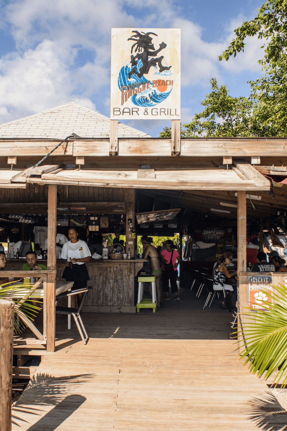 Relaxed beach bar and grill at Riggae Beach with ocean-themed signage and outdoor seating.
