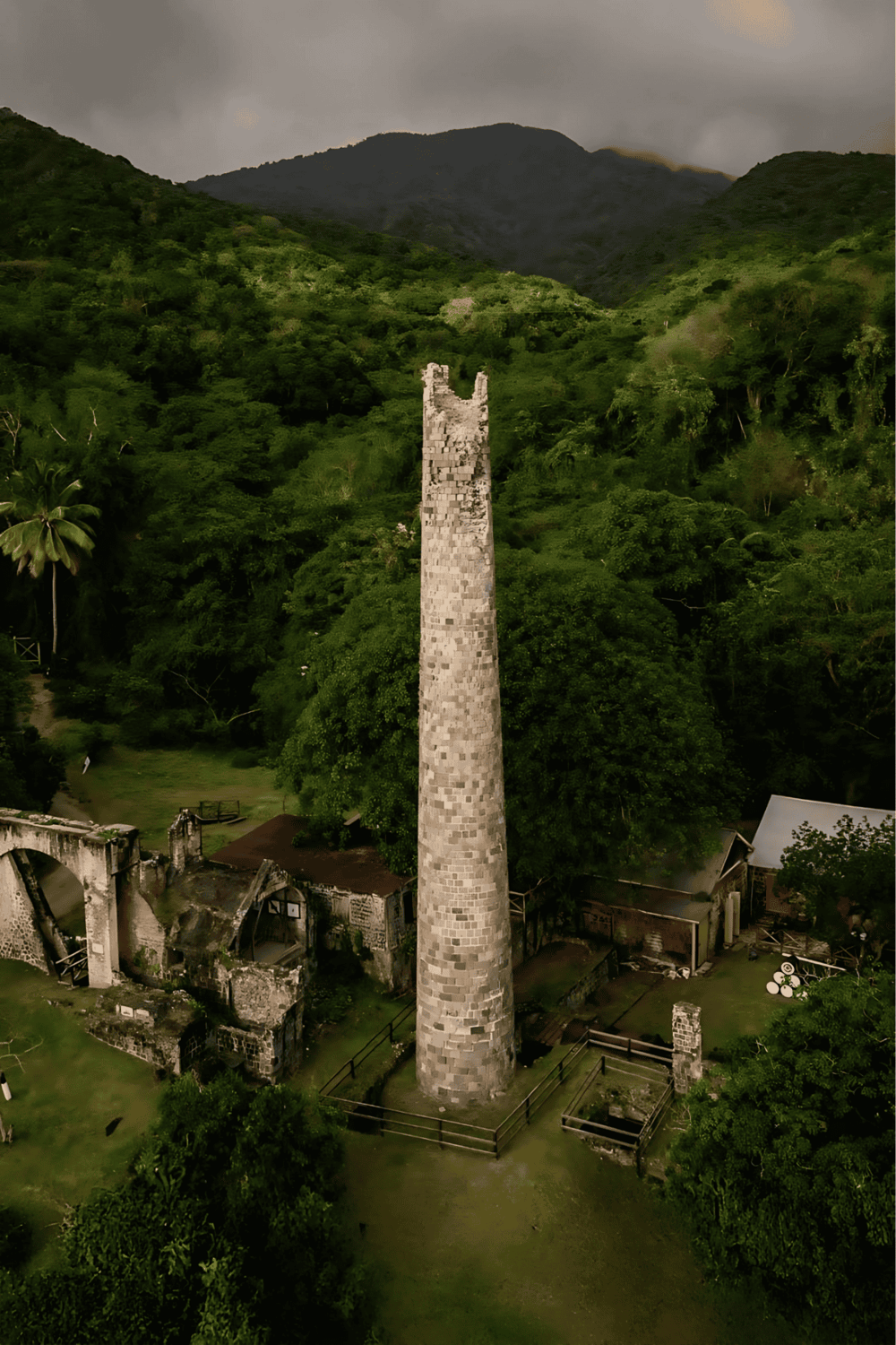 Ancient stone chimney in lush green jungle with mountains in background, historic ruins, and scenic landscape.